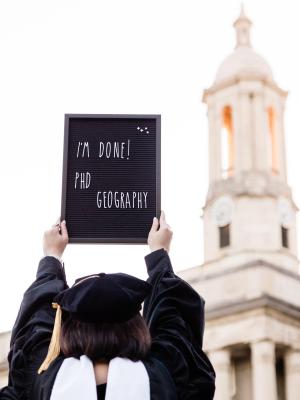 graduate holding a sign that says "I'm done PhD Geography"